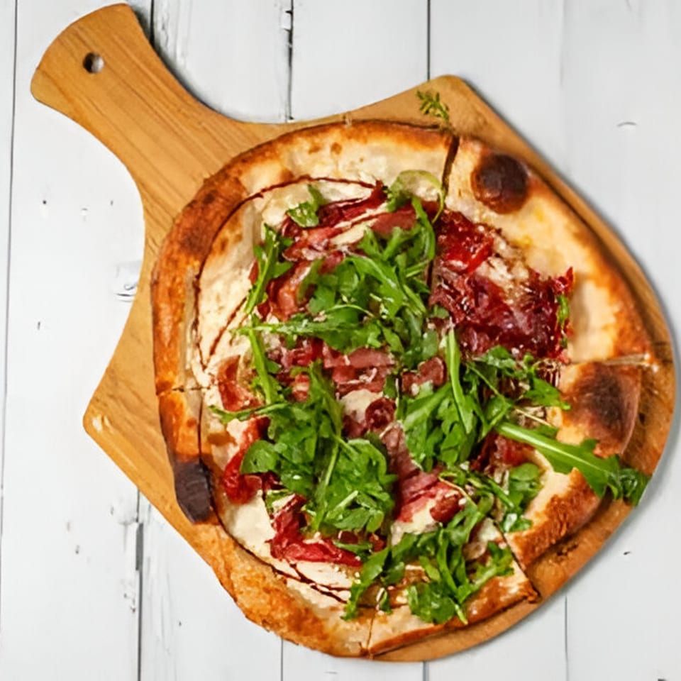 Mercer Village Pizza with prosciutto, arugula, and balsamic glaze on a wooden board.