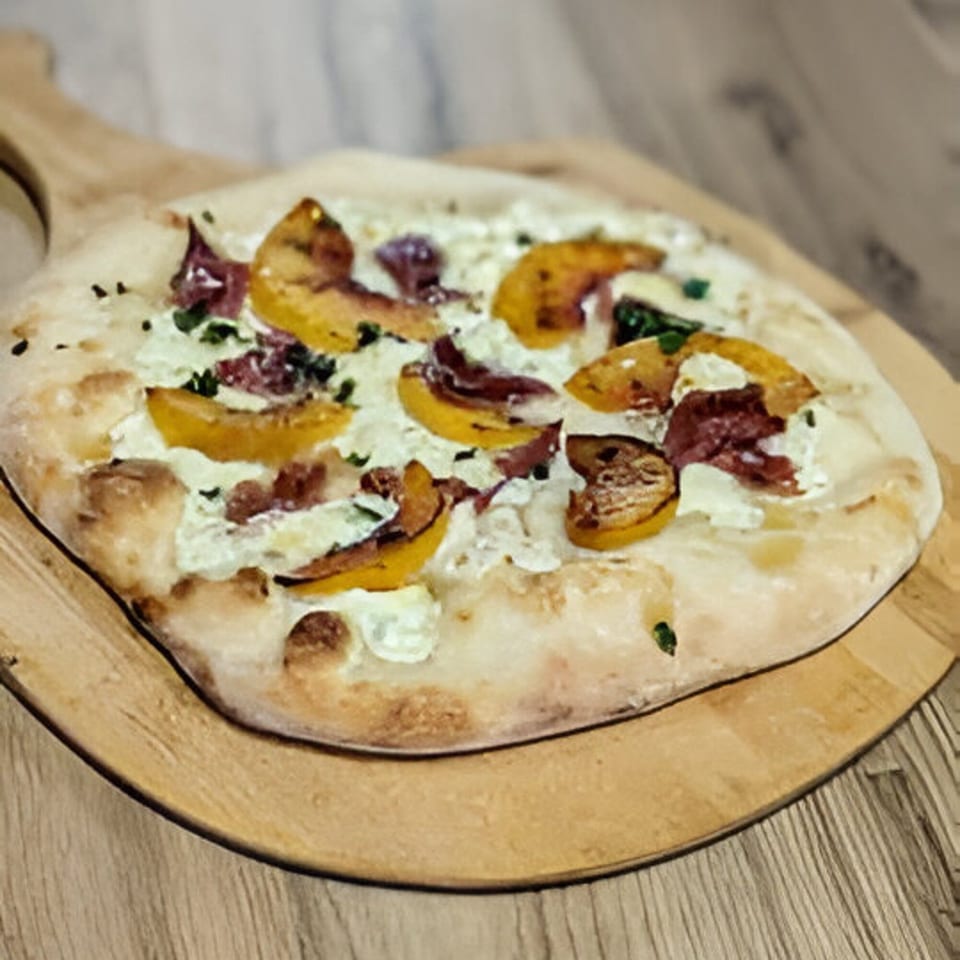 Mercer Village Pizza's white pizza with peaches and prosciutto on a wooden peel.