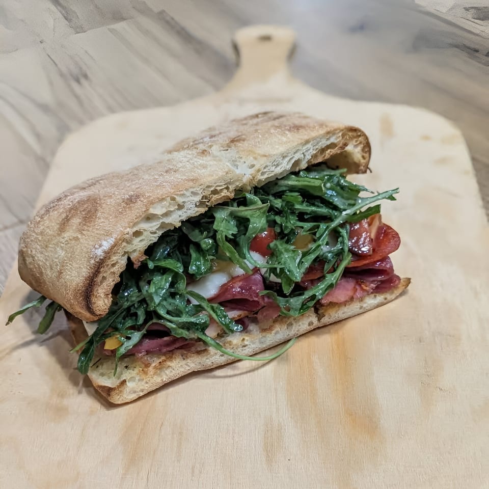 A delicious Mercer Village Pizza Inc. sandwich with arugula, tomatoes, and meat on a wooden board.