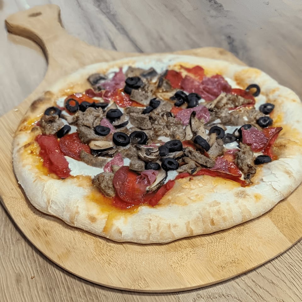 Mercer Village Pizza's pizza with sausage, pepperoni, olives, and red peppers on a wooden peel.