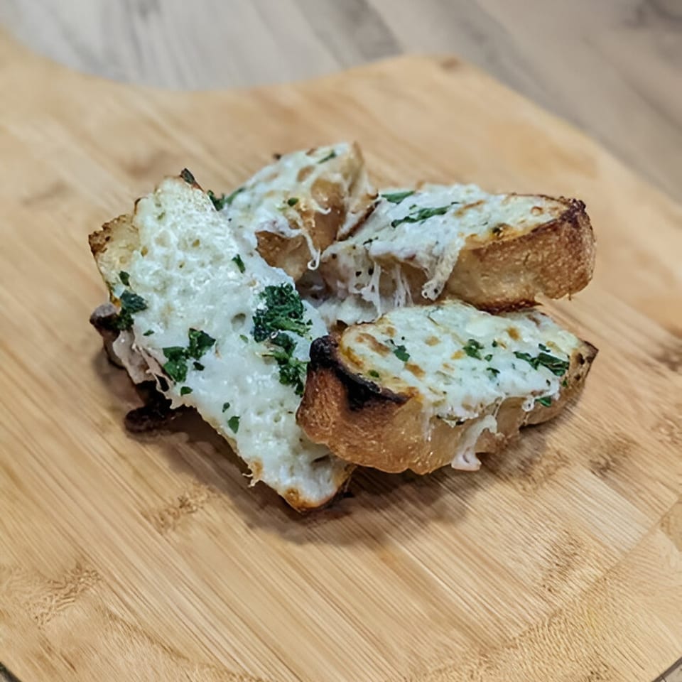 Four pieces of cheesy garlic bread with parsley on a wooden cutting board.