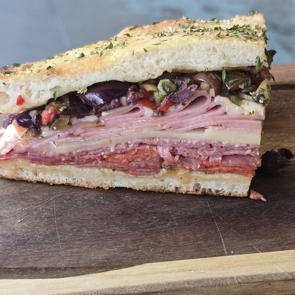 A large, thick slice of focaccia bread sandwich with layers of meats, cheeses, and olive salad.