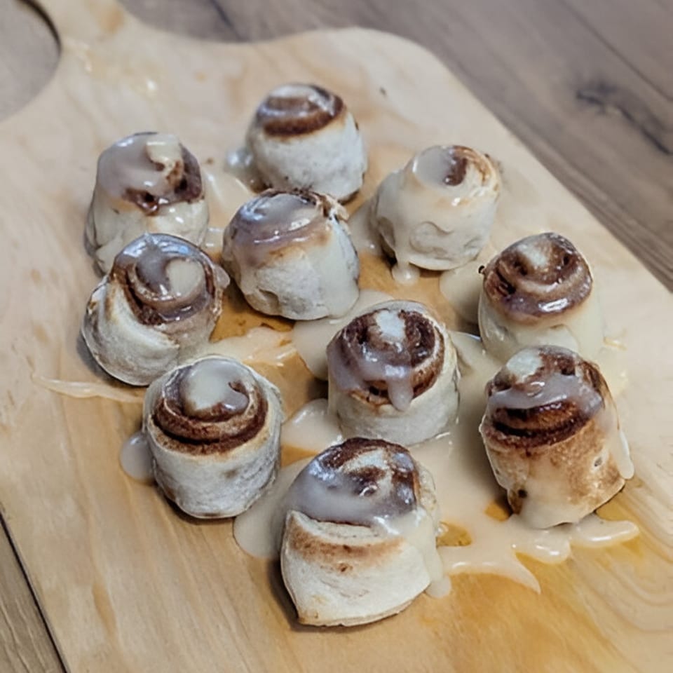 Nine mini cinnamon rolls with white icing on a light wooden board.